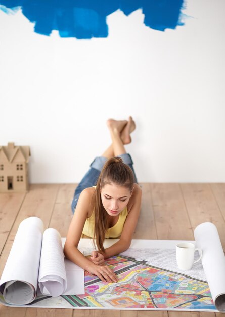 Jeune femme allongée sur le sol et regardant le plan de la nouvelle maison