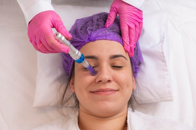 Jeune femme allongée sur la table du cosmétologue pendant la procédure de rajeunissement Le cosmétologue prend soin de la jeunesse et du bien-être de la peau du cou et du visage Procédure de nettoyage du visage du matériel