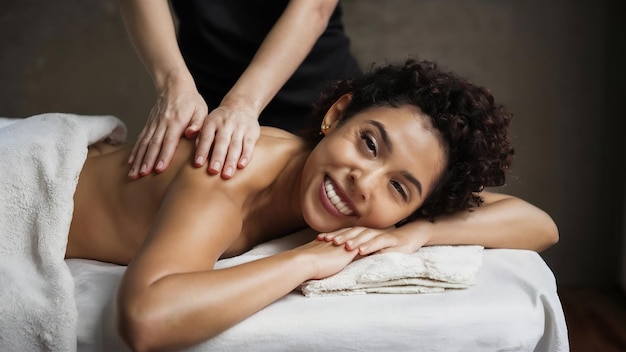 Une jeune femme allongée sur la table de massage et souriante.