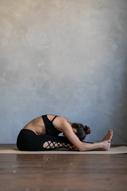 Jeune femme allongée sur un tapis de yoga. Fille se penchant sur ses pieds, pratique l'exercice d'étirement au cours de yoga.