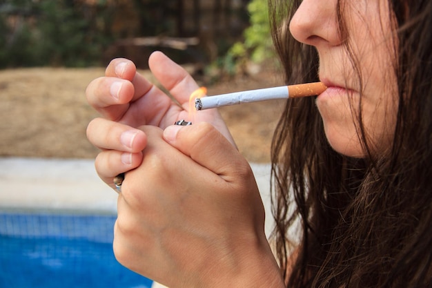 Jeune femme allumant une cigarette au bord de la piscine