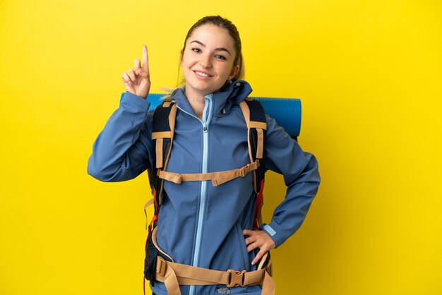 Jeune femme alpiniste avec un gros sac à dos sur fond jaune isolé pointant vers une excellente idée