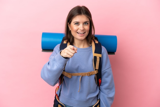 Jeune femme alpiniste avec un gros sac à dos isolé sur fond rose surpris et pointant vers l'avant