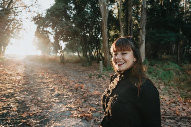 Jeune femme sur alternative noire portant souriant à la caméra sur une forêt avec une lumière vive à la fin. Concept d'avenir brillant et heureux, avenir du monde de la jeune femme.
