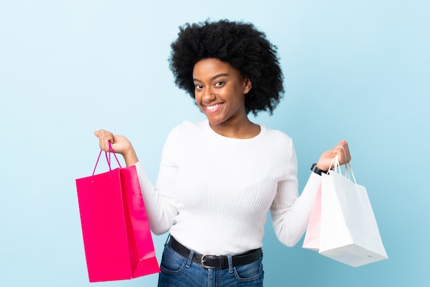 Jeune, femme américaine africaine, isolé, sur, mur bleu, tenue, sacs provisions, et, sourire