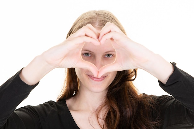 La jeune femme amoureuse forme un coeur avec ses doigts de main devant ses yeux de visage