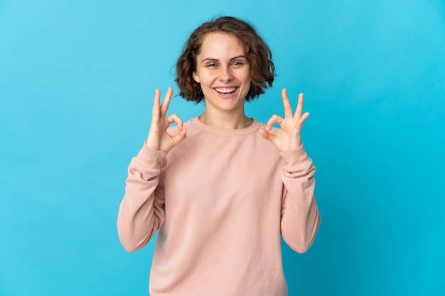 Jeune femme anglaise sur bleu montrant signe ok avec deux mains