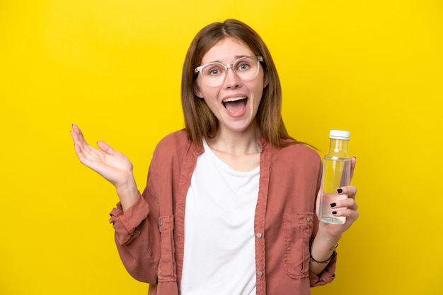 Jeune femme anglaise avec une bouteille d'eau isolée sur fond jaune avec une expression faciale choquée