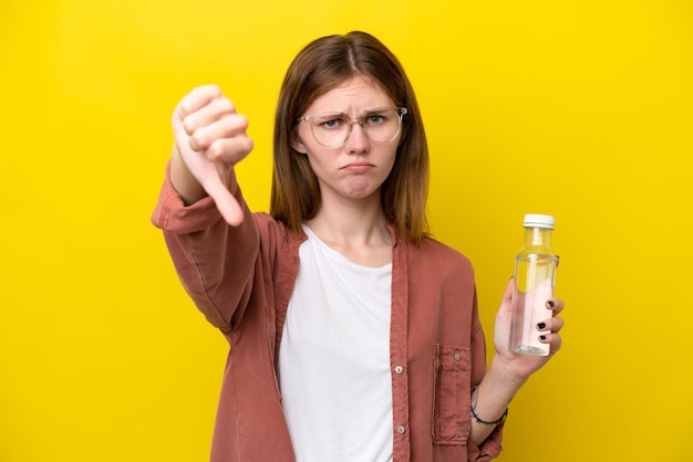 Jeune femme anglaise avec une bouteille d'eau isolée sur fond jaune montrant le pouce vers le bas avec une expression négative