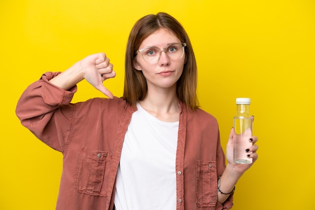 Jeune femme anglaise avec une bouteille d'eau isolée sur fond jaune montrant le pouce vers le bas avec une expression négative