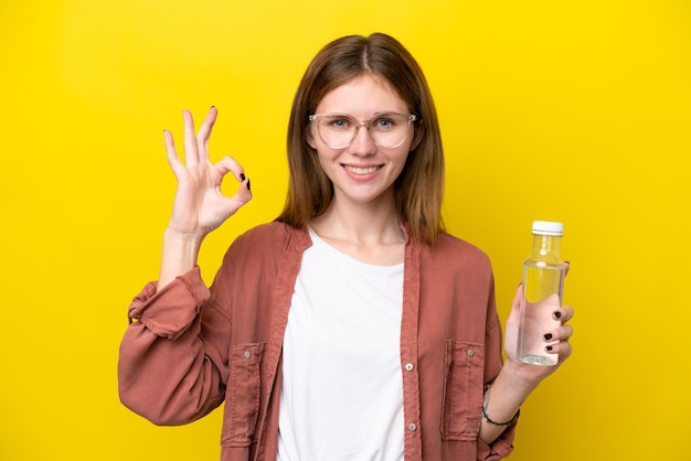 Jeune femme anglaise avec une bouteille d'eau isolée sur fond jaune montrant un signe ok avec les doigts