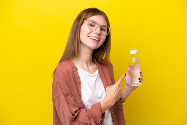 Jeune femme anglaise avec une bouteille d'eau isolée sur fond jaune pointant vers l'arrière