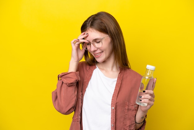 Jeune femme anglaise avec une bouteille d'eau isolée sur fond jaune en riant