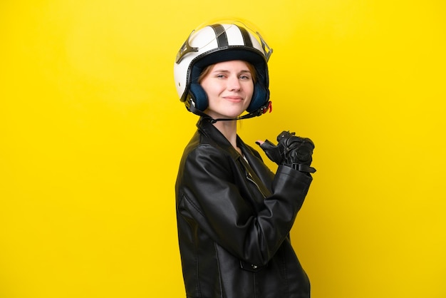 Jeune femme anglaise avec un casque de moto isolé sur fond jaune fière et satisfaite