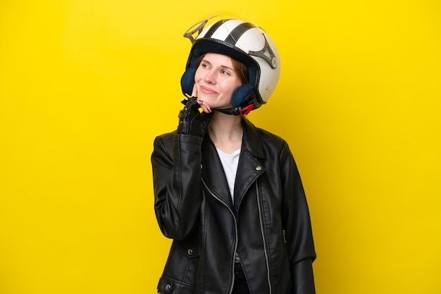 Jeune femme anglaise avec un casque de moto isolé sur fond jaune pensant à une idée tout en levant les yeux