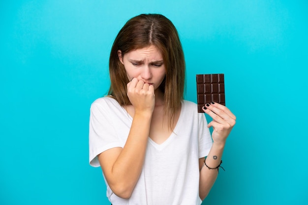 Jeune femme anglaise avec chocolat isolé sur fond bleu ayant des doutes