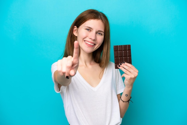 Jeune femme anglaise avec chocolat isolé sur fond bleu montrant et levant un doigt