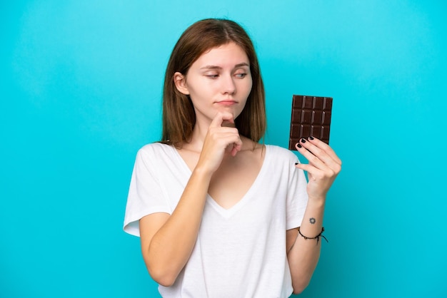 Jeune femme anglaise avec du chocolat isolé sur fond bleu ayant des doutes et pensant