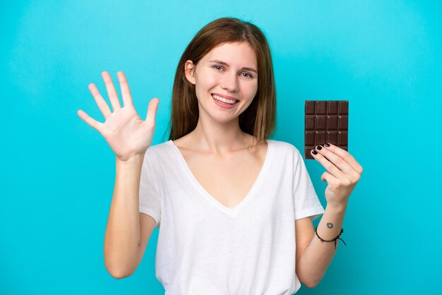 Jeune femme anglaise avec du chocolat isolé sur fond bleu comptant cinq avec les doigts