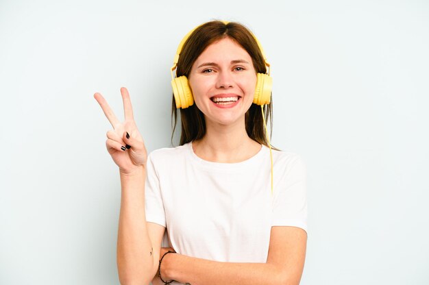 Jeune femme anglaise écoutant de la musique isolée sur fond bleu montrant le numéro deux avec les doigts.