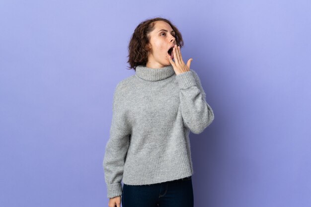 Jeune femme anglaise sur fond violet bâillant et couvrant la bouche grande ouverte avec la main