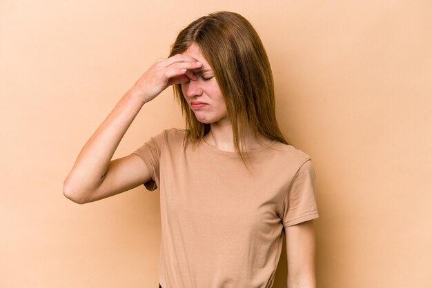 Jeune femme anglaise isolée sur fond beige ayant un mal de tête touchant l'avant du visage