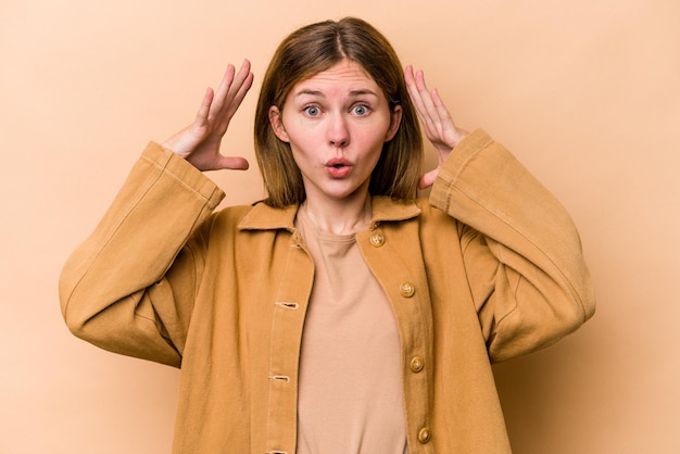 Jeune femme anglaise isolée sur fond beige célébrant une victoire ou un succès, il est surpris et choqué