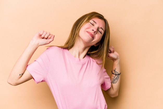 Jeune femme anglaise isolée sur fond beige étirant les bras en position détendue