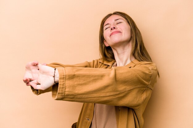 Jeune femme anglaise isolée sur fond beige étirant les bras en position détendue