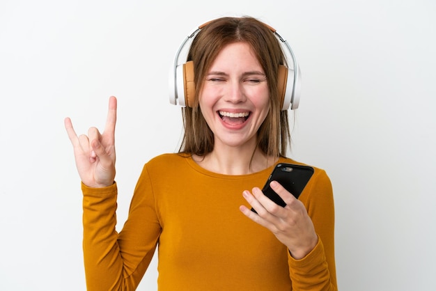 Jeune femme anglaise isolée sur fond blanc écoutant de la musique avec un mobile faisant un geste rock