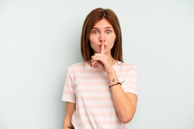 Jeune femme anglaise isolée sur fond bleu gardant un secret ou demandant le silence.