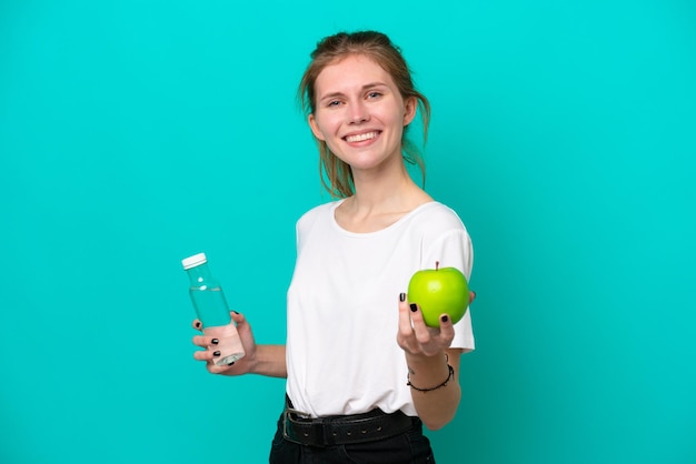 Jeune femme anglaise isolée sur fond bleu avec une pomme et une bouteille d'eau