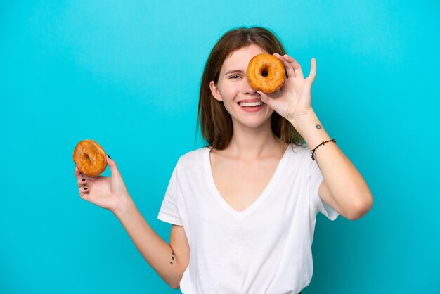 Jeune femme anglaise isolée sur fond bleu tenant un beignet et heureux