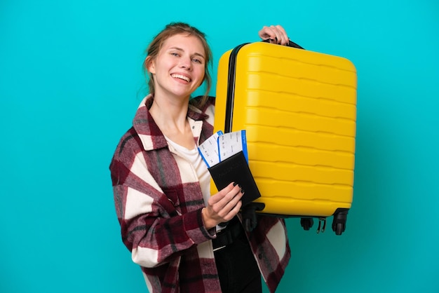 Jeune femme anglaise isolée sur fond bleu en vacances avec valise et passeport