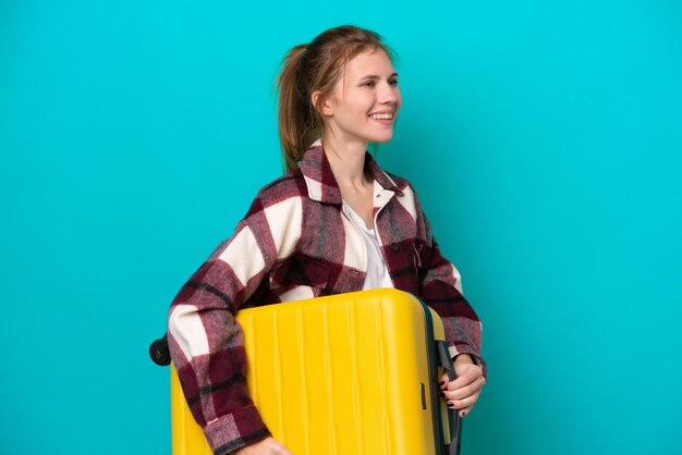 Jeune femme anglaise isolée sur fond bleu en vacances avec valise de voyage