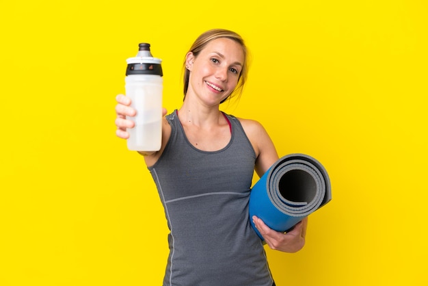 Jeune femme anglaise isolée sur fond jaune avec une bouteille d'eau de sport et avec un tapis