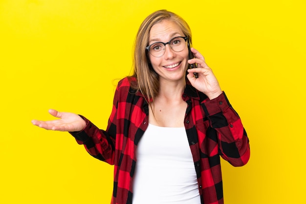 Jeune femme anglaise isolée sur fond jaune gardant une conversation avec le téléphone portable avec quelqu'un