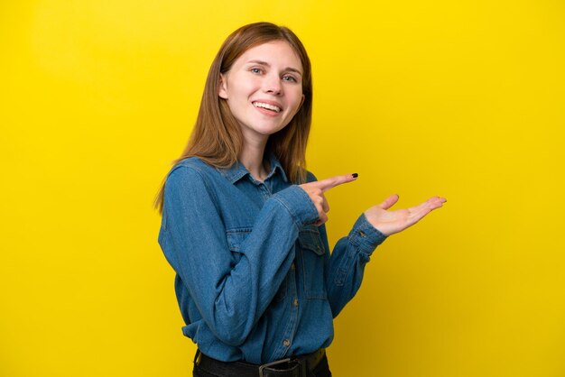 Jeune femme anglaise isolée sur fond jaune tenant un espace de copie imaginaire sur la paume pour insérer une annonce