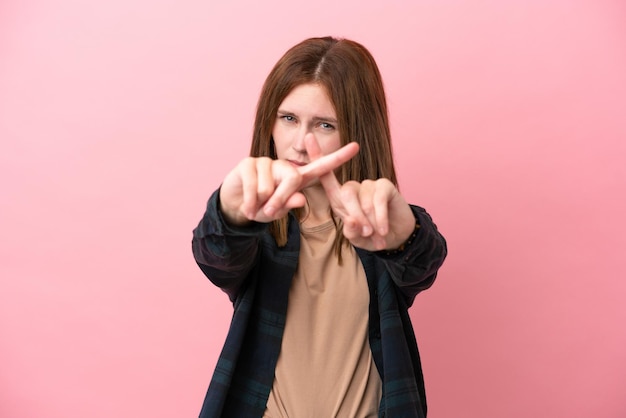 Jeune femme anglaise isolée sur fond rose faisant un geste d'arrêt avec sa main pour arrêter un acte