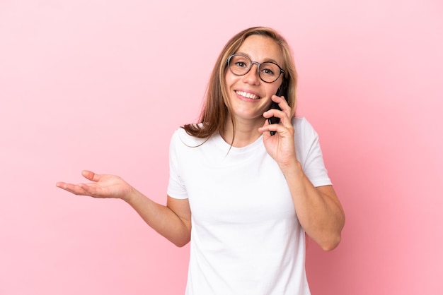 Jeune femme anglaise isolée sur fond rose en gardant une conversation avec le téléphone portable avec quelqu'un