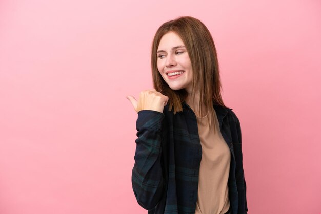 Jeune femme anglaise isolée sur fond rose pointant vers le côté pour présenter un produit