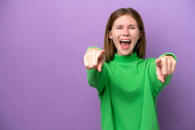 Jeune femme anglaise isolée sur fond violet surpris et pointant vers l'avant