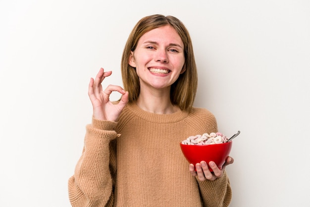 Jeune femme anglaise mangeant des céréales isolées sur fond blanc gaie et confiante montrant un geste ok.
