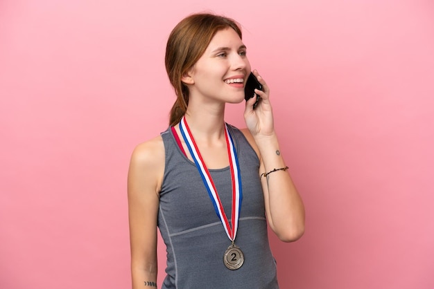 Jeune femme anglaise avec des médailles isolées sur fond rose en gardant une conversation avec le téléphone mobile