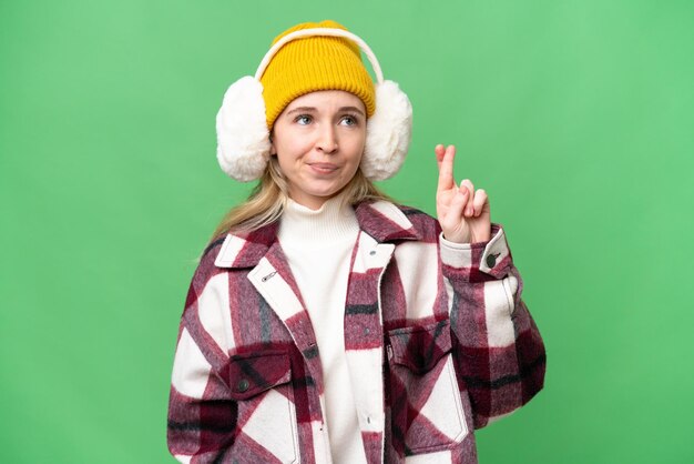 Jeune femme anglaise portant des manchons d'hiver sur fond isolé avec les doigts croisés et souhaitant le meilleur