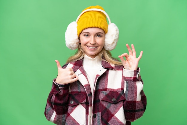 Jeune femme anglaise portant des manchons d'hiver sur fond isolé montrant le signe ok et le geste du pouce vers le haut