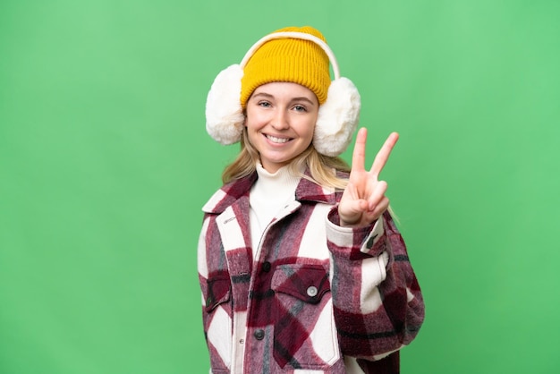 Jeune femme anglaise portant des manchons d'hiver sur fond isolé souriant et montrant le signe de la victoire
