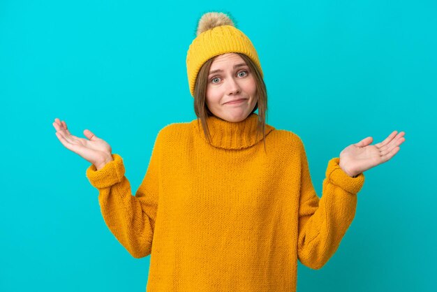 Jeune femme anglaise portant une veste d'hiver isolée sur fond bleu ayant des doutes tout en levant les mains