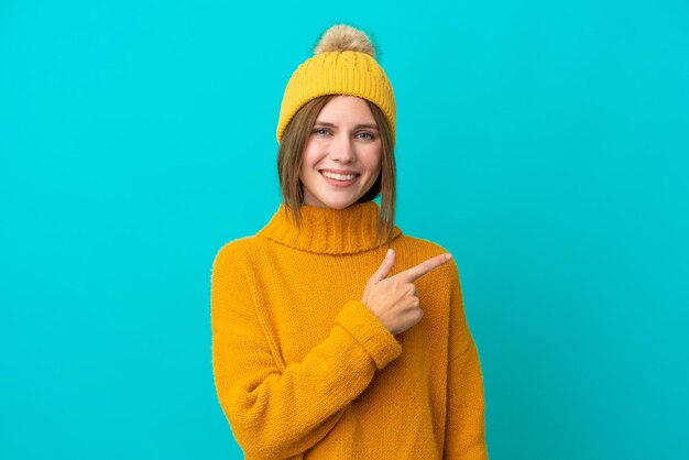 Jeune femme anglaise portant une veste d'hiver isolée sur fond bleu pointant vers le côté pour présenter un produit