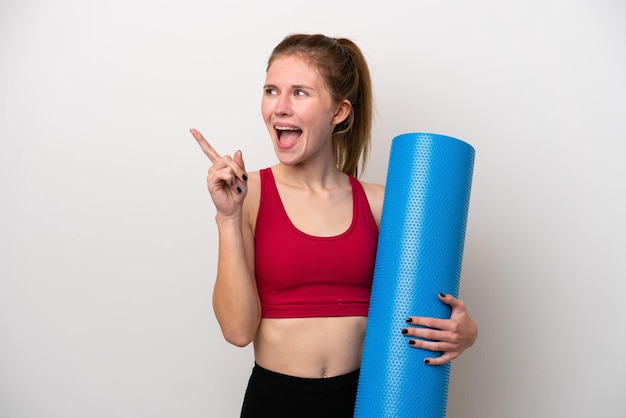 Jeune femme anglaise sportive allant à des cours de yoga tout en tenant un tapis isolé sur fond blanc dans l'intention de réaliser la solution tout en levant un doigt